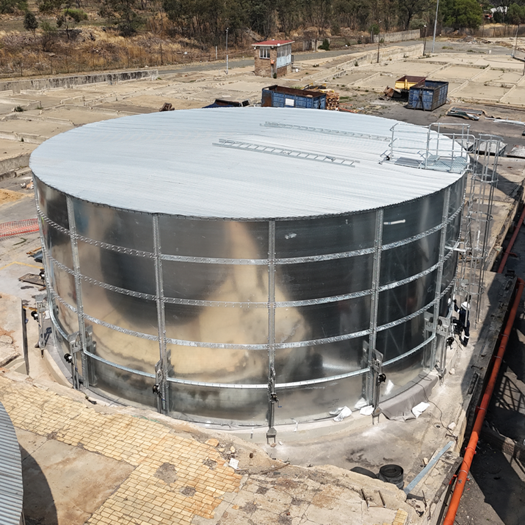 Cylindrical steel water storage tank with ladder and corrugated roof, installed on a concrete base.