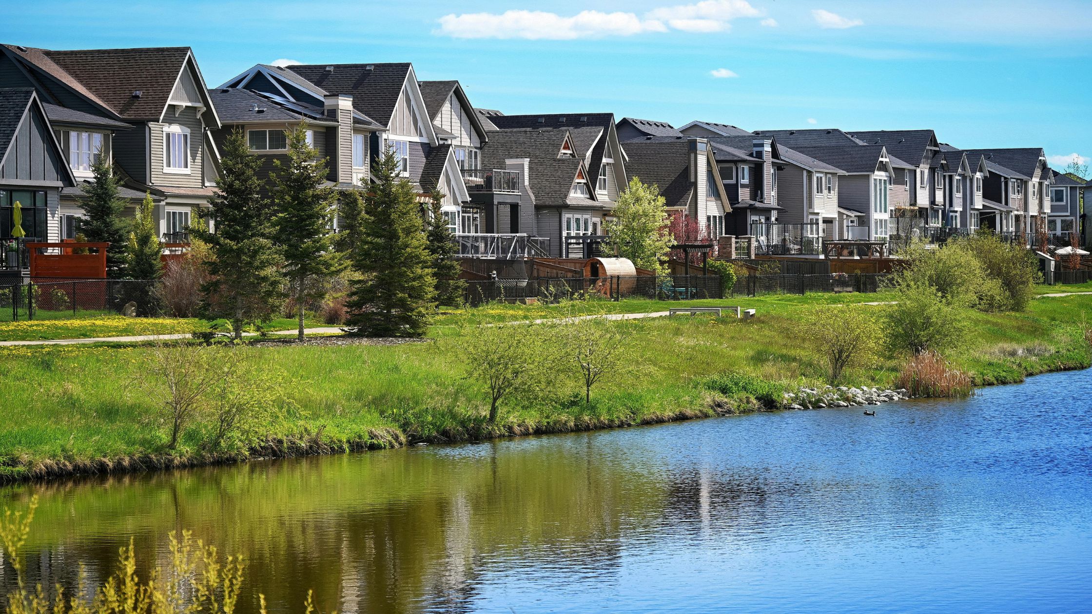 Row of retirement-style houses alongside a calm pond, representing eco-friendly and serene senior living environments.