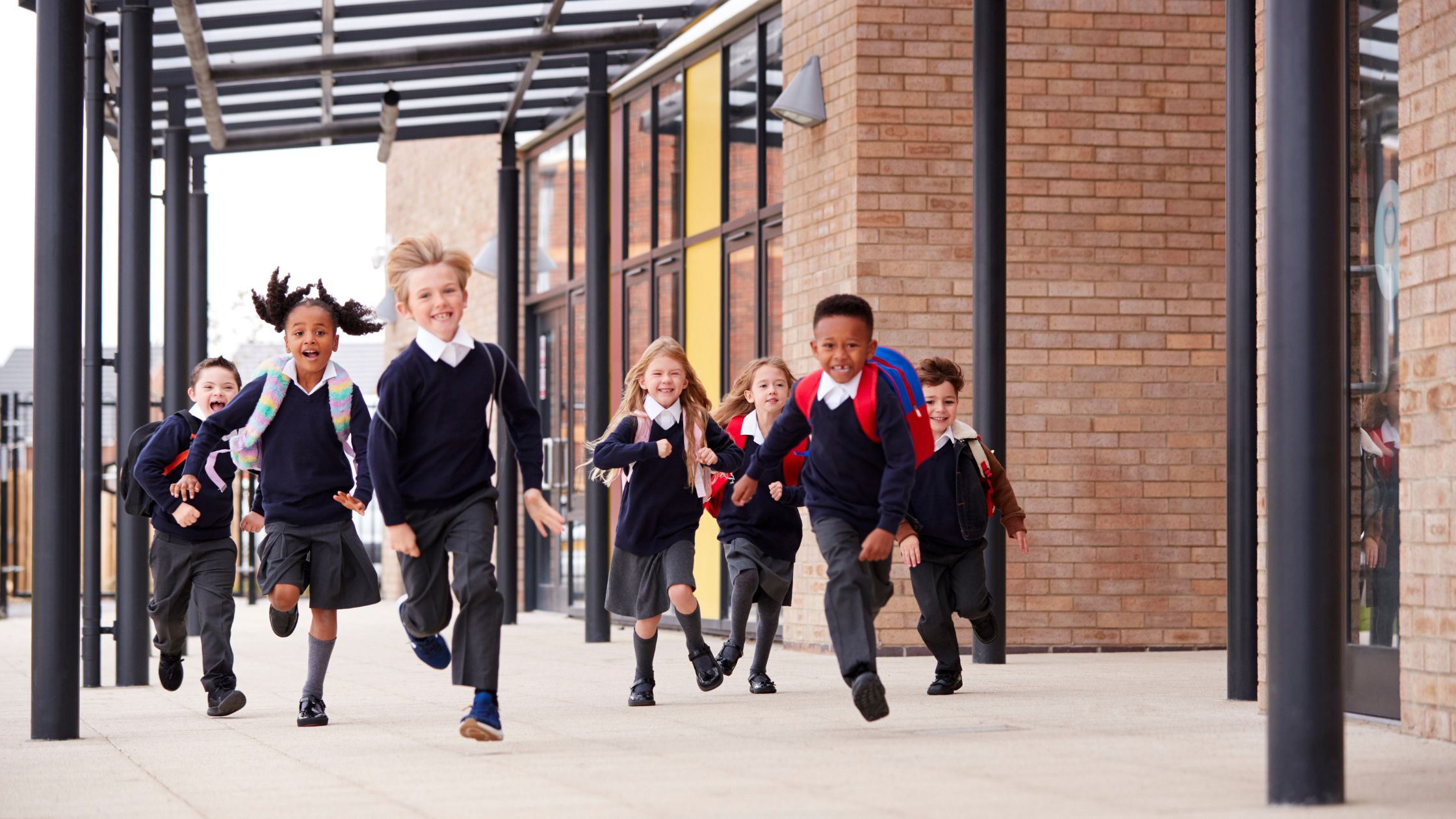 Group of school children in uniform running outside a modern school building, representing the need for reliable water in safe learning environments.