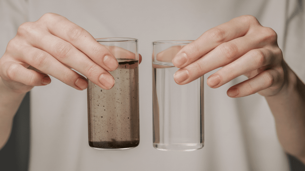 Hands holding two glasses—one with dirty water and one with clean, treated water—highlighting the impact of purification.
