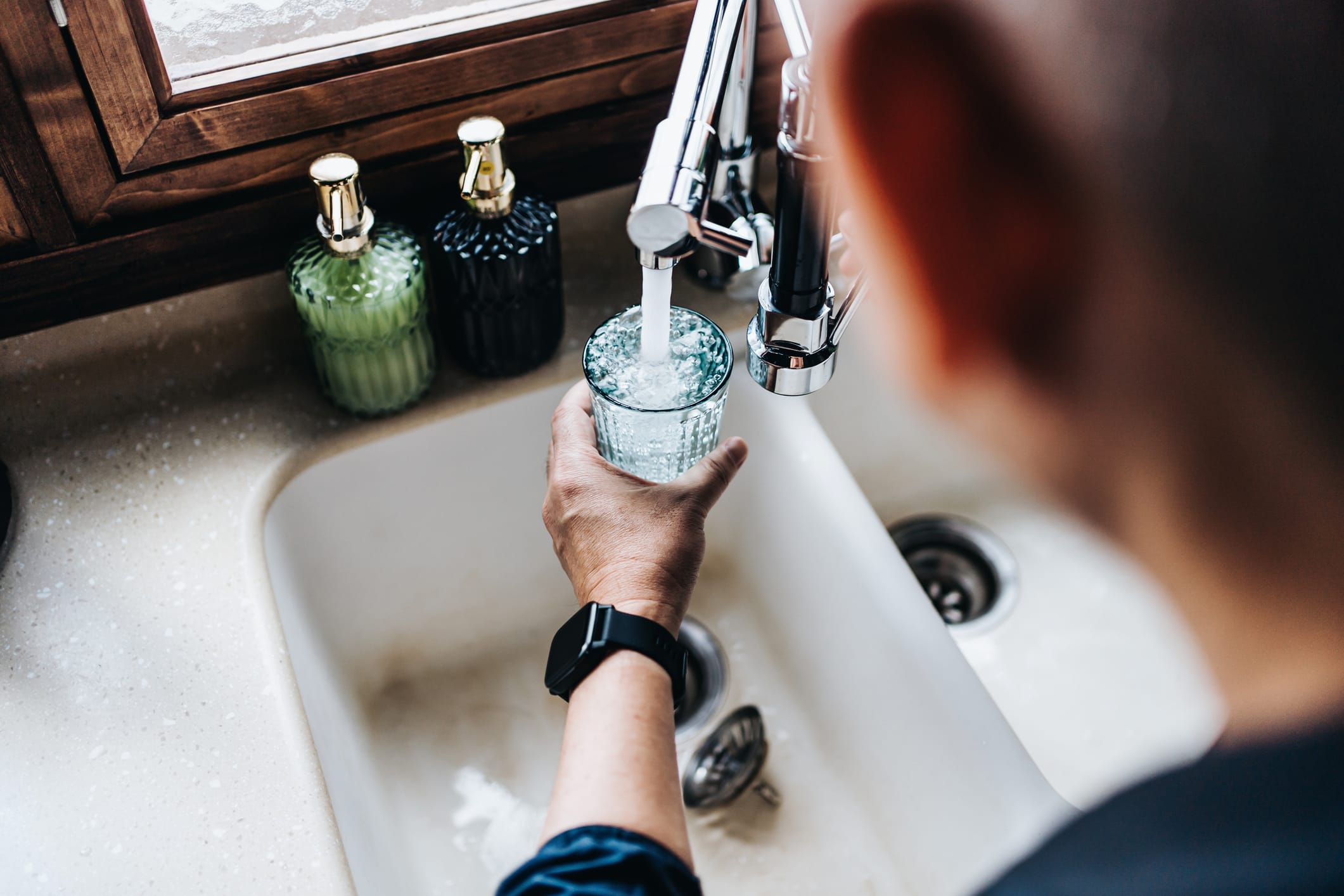 Over the shoulder view of senior Asian man filling a glass of filtered water right from the tap in the kitchen at home Water sample being collected for SANS 241 drinking water quality testing in Cape Town.